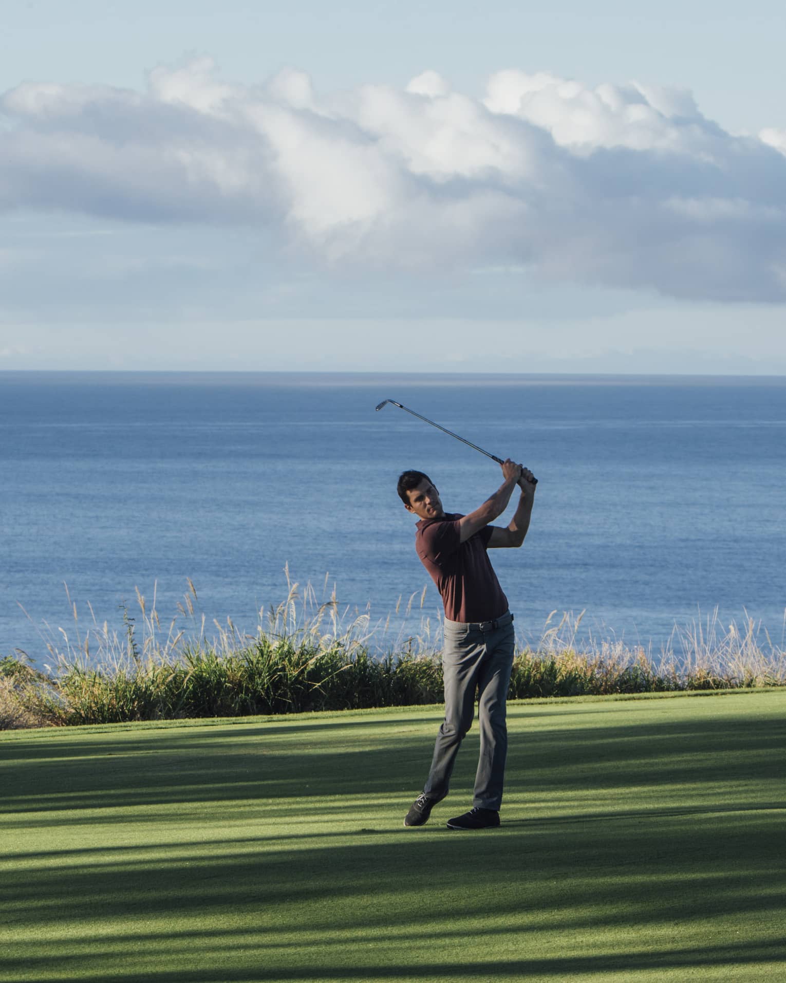 Man swings club on golf course green by ocean